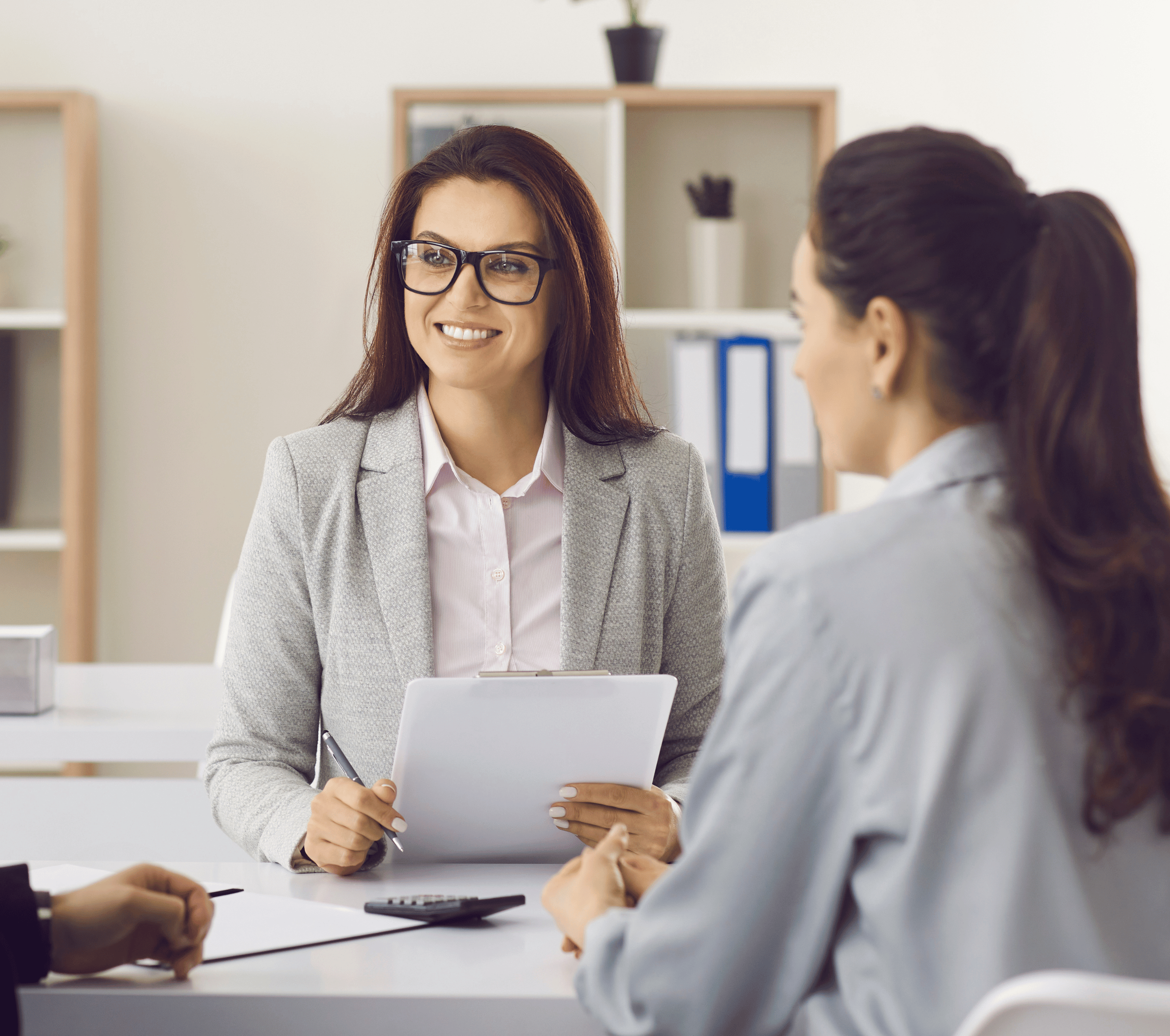 Office woman sitting at table across from another woman smiling and holding paper work in office room explaining personal injury claims